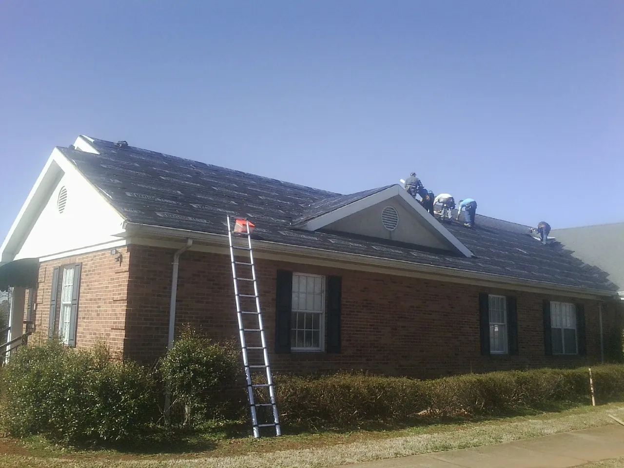 Crew tearing shingles off a brick ranch roof with a ladder set — Emergency Roof Repair work by our crew in Deer Park